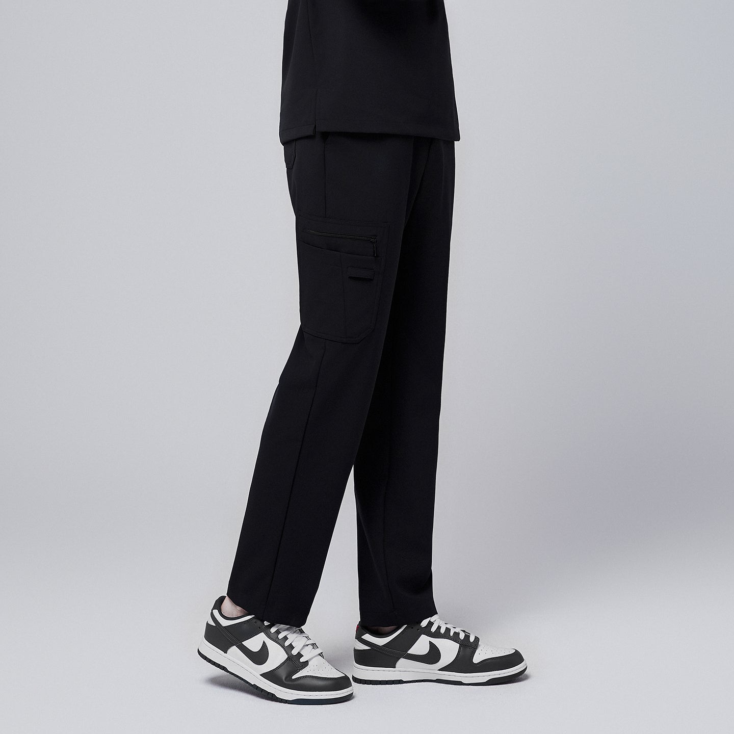 Image of Male model showcasing jet black relaxed-fit scrub pants with functional side pocket design, paired with black and white sneakers, highlighting a professional yet comfortable style,Jet Black